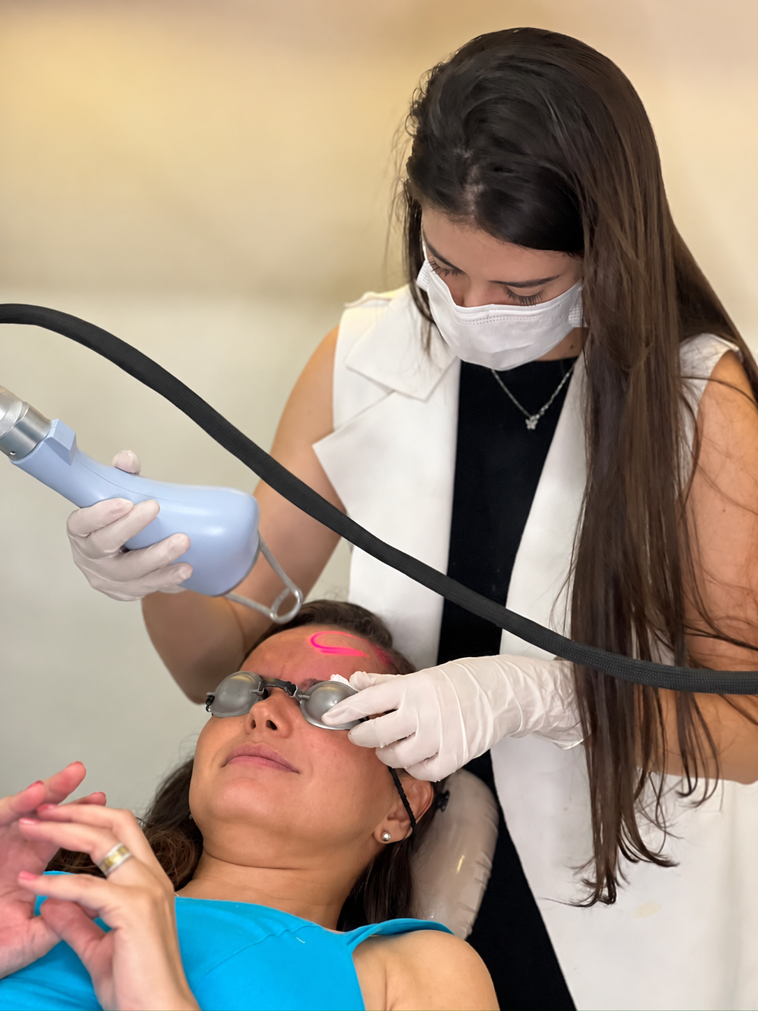 Leticcia realizando atendimento estético com equipamento e proteção ocular